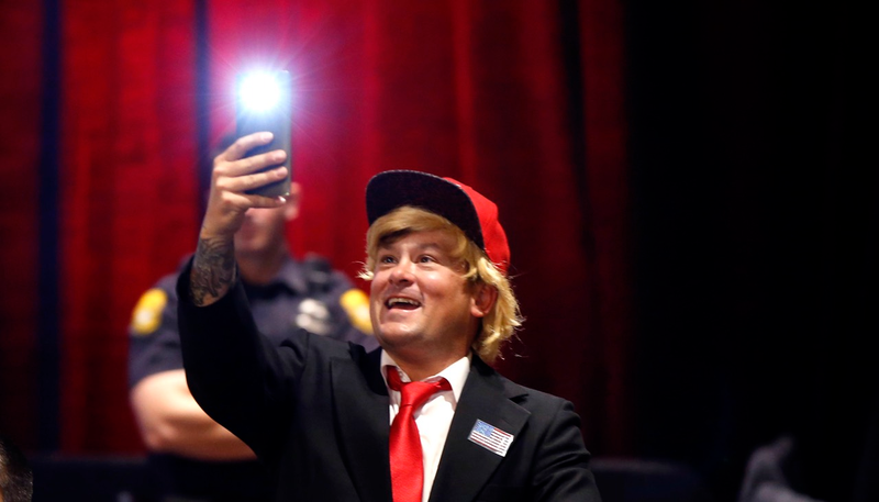 A man dressed like Republican presidential candidate Donald Trump takes a photo of himself before Trump arrives at a campaign event (Associated Press)